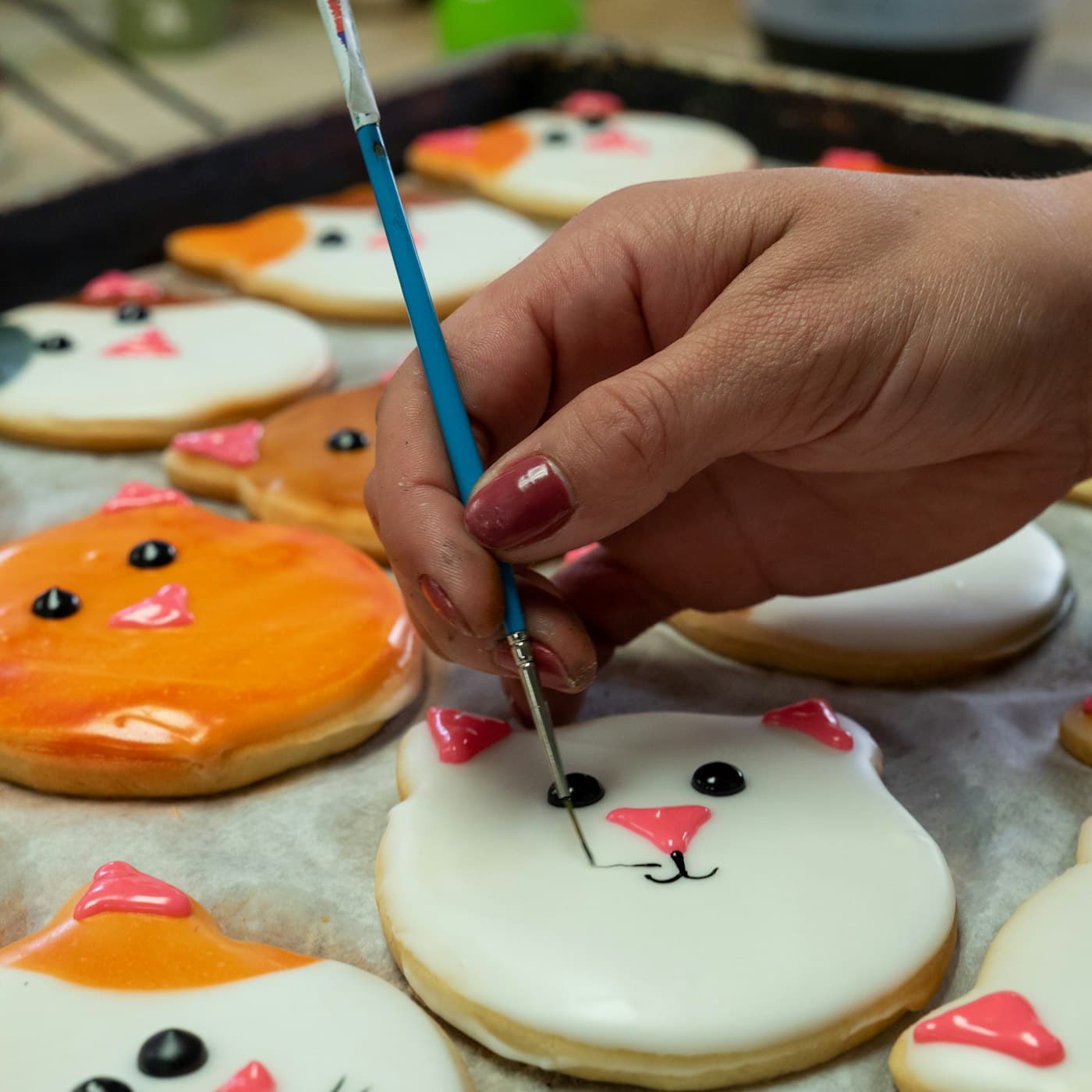 Mano pintando con pincel una galleta glaseada en forma de gato