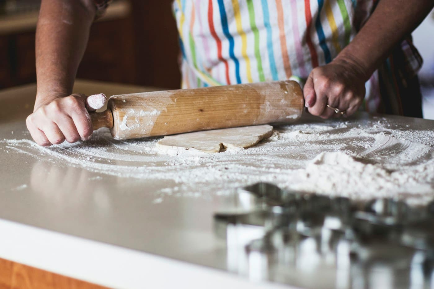 Manos estirando masa con un rodillo junto a cortadores de galletas